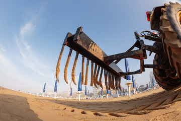 Fototapeta premium tractor on the sandy beach cleaning, after winter, preparation for the holiday season in Italy. Wooden trunks in on the seashore after a sea storm. dense sea breeze at dawn