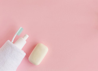 Toothbrushes and toothpaste wrapped in white towel near soap on pink background. Dental and healthcare concept. Free copy space.