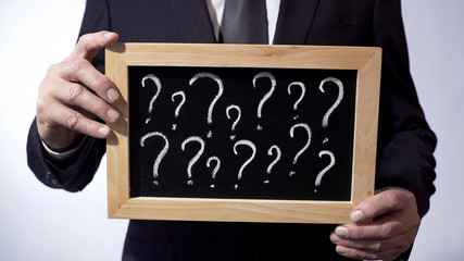 Question marks written on blackboard, male wearing classic suit holding a sign