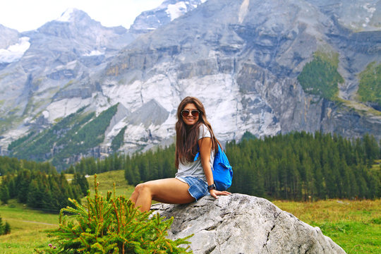 Happy Young Woman Tourist In Glasses, Shorts And Sneakers With A Backpack Travels In The Mountains And Enjoys The Summer Forest Landscape, Frundenhutte Oeschinen Lake, Switzerland, Alps