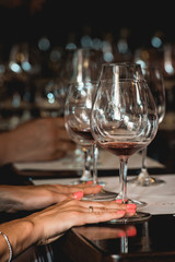 woman holds glass of red wine. people consider the color of the wine and try how it smells in different glasses