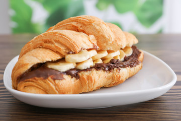 Tasty croissant with banana and chocolate sauce on plate, closeup