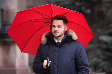 Young man in warm clothes with red umbrella outdoors