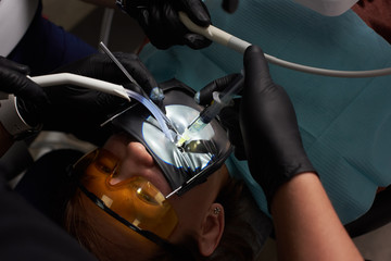 Dentist performs dental treatment by putting an injection to a smiling patient in orange dental glasses
