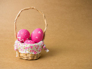 Easter eggs in a basket weave wood on the left corner on a brown background.
