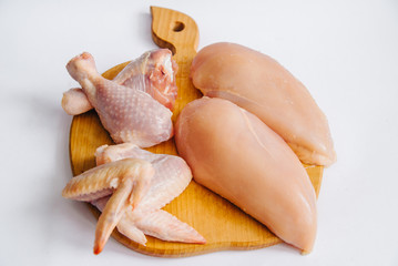 Raw chicken fillets, chicken legs and chicken wings on wooden cutting board, on white background, top view, for a picnic