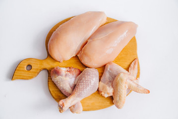 Obraz na płótnie Canvas Raw chicken fillets, chicken legs and chicken wings on wooden cutting board with lettuce leaves, on white background, top view