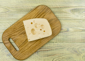 A piece of cheese with large holes on a wooden cutting board.