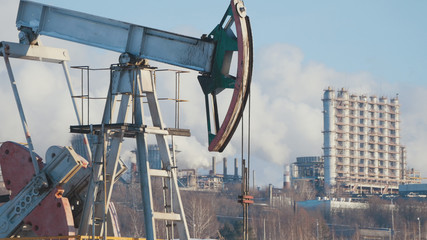 Close-up of a working pump for the extraction of crude oil and of a petrochemical plant's pipes...