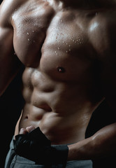 Athletic body of a man with tight muscles and drops of water on the skin on a black isolated background.