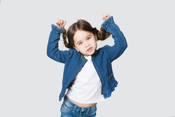 Funny little girl  in jeans looking at camera  over white background.