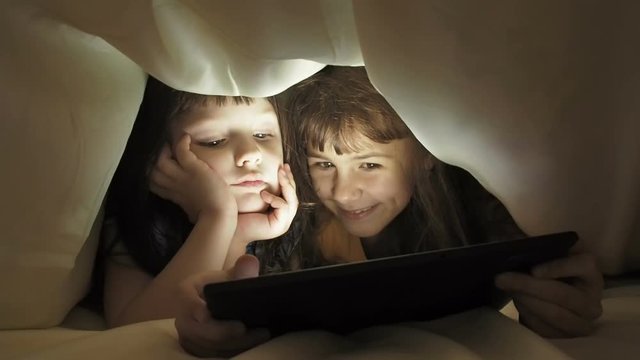Children on the Internet. Little girls under the blanket with a tablet.