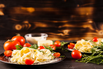 Healthy delicious pasta next to tomatoes, greenery and parmesan on wooden background