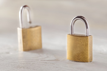 Fototapeta premium Two padlock, lock and unlock, with silvered keys on white wooden background. Estate and security concept with symbol of protection.