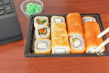 Quick lunch at work - lack of time out of the office. Sushi rolls with wasabi at workplace. Workplace with notebook. Working and lifestyle concept