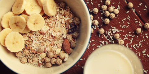 Healthy breakfast. Granola bowl with banana, raisins and nuts. And a glass of milk on the wooden background. Top view. Close up photo. Sweet vegan dish. Morning oatmeal closeup.