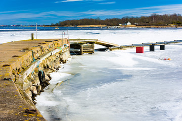 Warm and sunny spring day on the island of Hasslo, Sweden. The ice is thawing beside the pier and in the background, you can see part of Karlskrona city and a coastal home on the island.