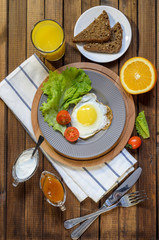 English Breakfast: fried egg, juice, cherry tomatoes, lettuce, grain bread, sauce, top view.