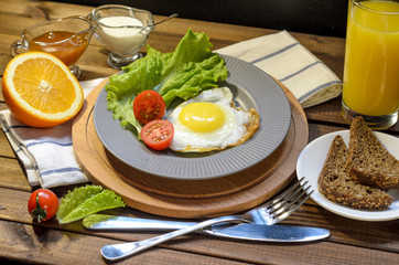 English Breakfast: fried egg, juice, cherry tomatoes, lettuce, grain bread, sauce, top view.