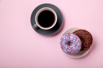 Glazed berry and chocolate donuts with sweet sprinkles on pink background with a cup of black coffee