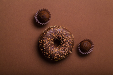 Chocolate donuts with chocolate truffles on brown background. Monochromatic concept.