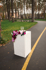 Two glasses with champagne stand on a pedestal decorated with flowers in the park. Wedding details