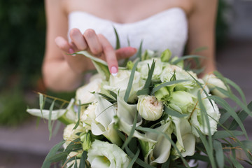 Lush bridal bouquet with white flowers and a lot of greenery. Bride touching wedding bouquet. Wedding details