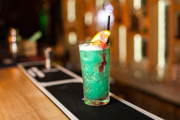Green, turquoise cocktail with lemon and streaks of syrup in bar