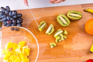 Woman cut kiwi on a wooden cutting board for a vegan fruit salad, close-up - female hands, healthy eating concept