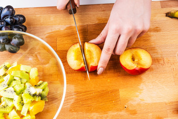 Woman cutting a plum for fruit salad on a wooden cutting board close-up