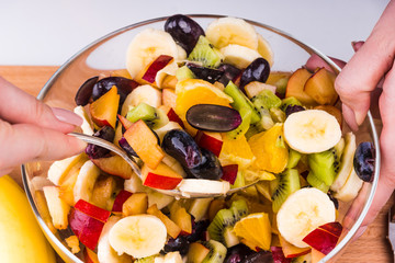Woman mixing a vegan fruit salad in a glass bowl - close-up, concept of a healthy lifestyle
