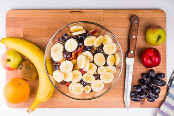 Glass bowl with fruit salad and ingredients on a wooden board - top view, concept of low-calorie diet