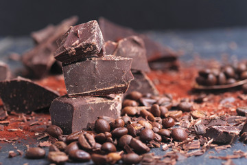 Broken dark chocolate, cocoa powder and coffee beans on a wooden table