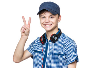 Portrait of young student with cap and headphones. Teenager smiling, making victory gesture and looking at camera. Happy teen boy, isolated on white background.