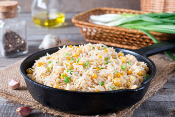 Asian fried rice with eggs and corn in a frying pan on wooden background
