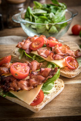 Ciabatta sandwich with arugula salad, bacon and yellow cheese.