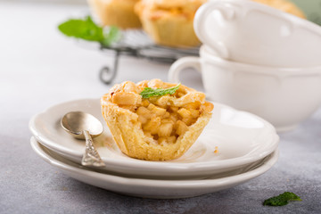 Homemade mini apple pies on white plates decorated with mint leaves on light concrete background. Healthy food concept.