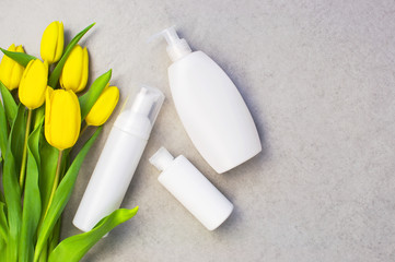 Bottles products for shower and bathroom on a gray background with yellow flowers tulips. Set of cosmetic bottles with space for text. Shampoo, liquid soap, shower gel. Top view. Flat lay.