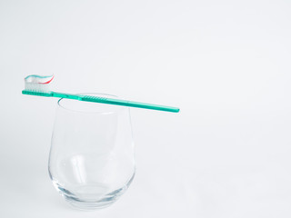 A toothbrush is lying on the glass and toothpaste has been applied against a white background