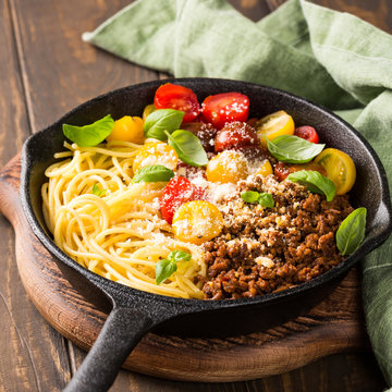 Healthy italian food. Delicious spaghetti Bolognaise or Bolognese with savory minced beef and cherry tomatoes garnished with parmesan cheese and basil in cost iron pan. Copy space.