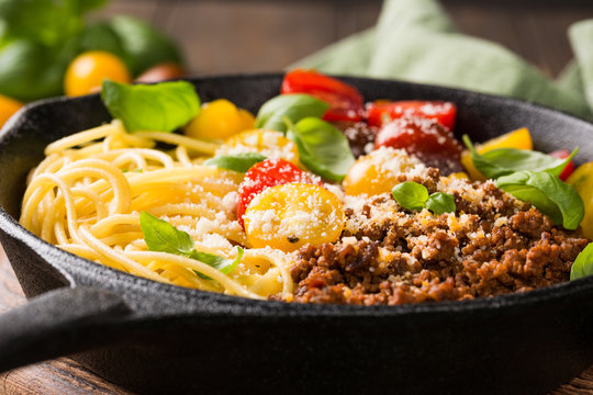 Delicious spaghetti Bolognaise or Bolognese with savory minced beef and cherry tomatoes garnished with parmesan cheese and basil in cost iron pan. Healthy italian food. Close up.