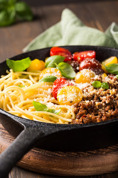 Delicious spaghetti Bolognaise or Bolognese with savory minced beef and cherry tomatoes garnished with parmesan cheese and basil in cost iron pan. Healthy italian food. Copy space.
