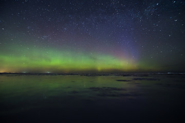 Night sky view of beautiful green aurora borealis (northern polar lights) in Finland with reflection on the frozen lake during geomagnetic storm at expedition