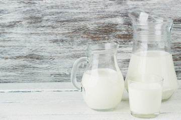 Milk in the glass jugs on the wooden background