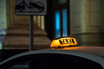 Illuminated taxi sign on the roof of a taxi at night city