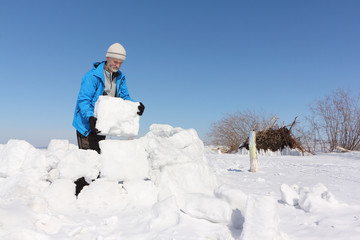 Man in a blue jacket building an igloo on a glade in the winter
