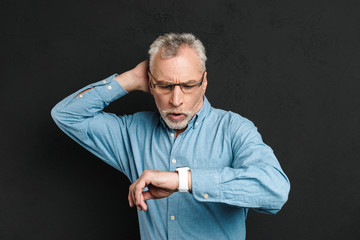 Image of elderly unshaved man 60s with grey hair wearing eyeglasses looking at his wrist watch with...