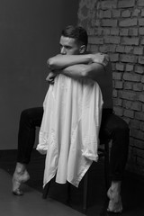 white young guy sitting on a chair near a gray brick wall, black-and-white photo