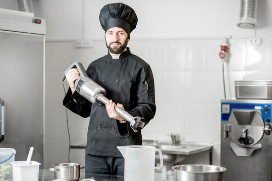 Portrait of a chef cook standing with blender in the professional kitchen during the process of ice cream making