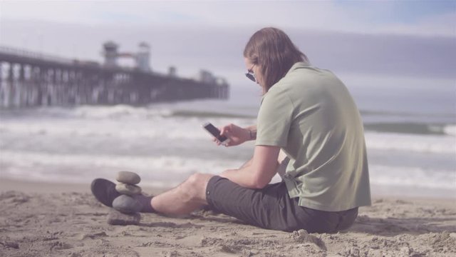 Young man relaxing at the beach while using his cellphone